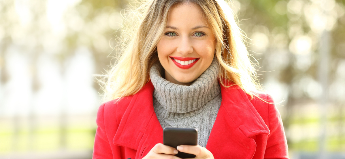 Smiling woman in red coat holding a cell phone.